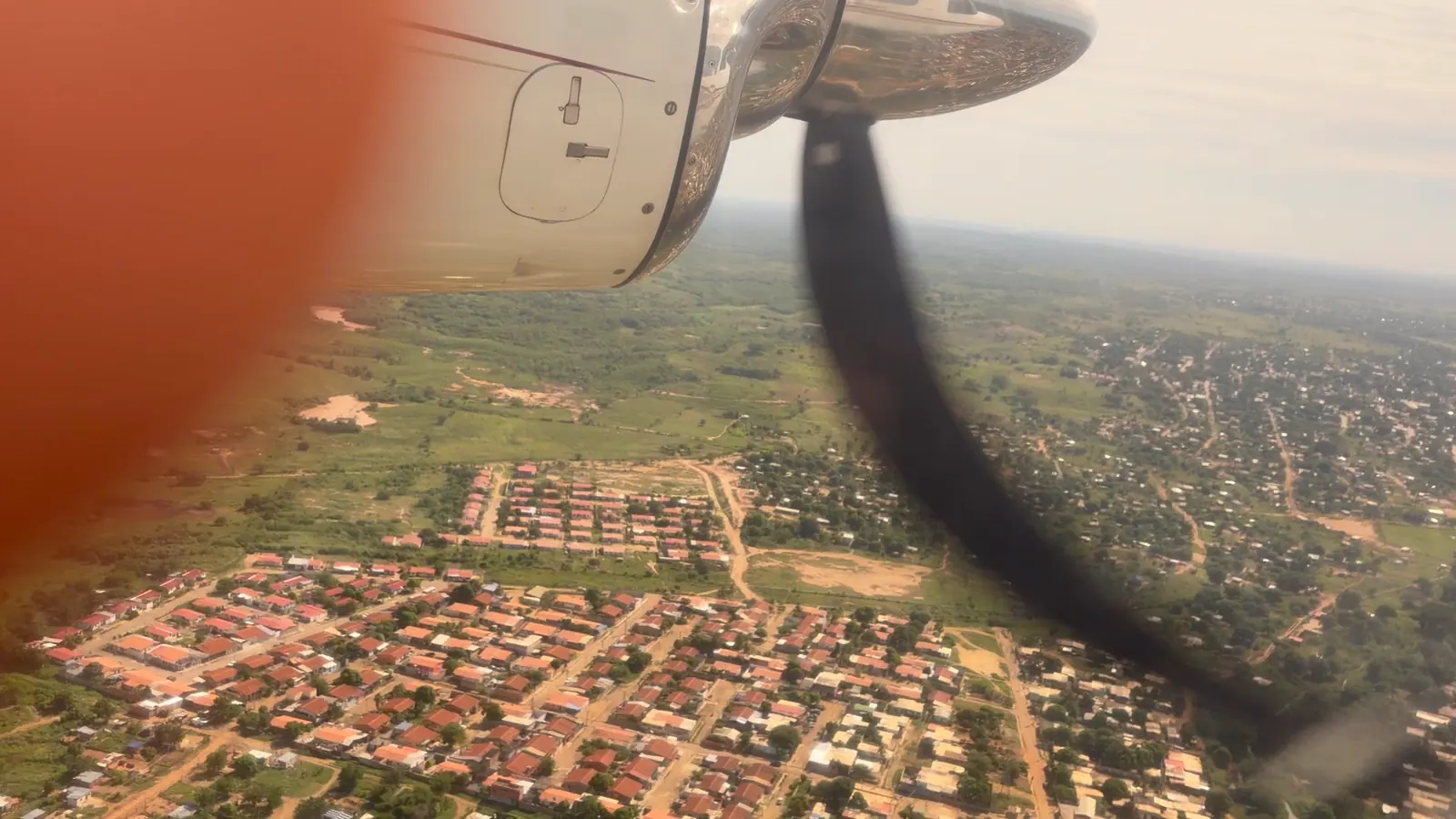 Vista de campos y una población desde la ventana de un avión, con el motor y la hélice visibles.