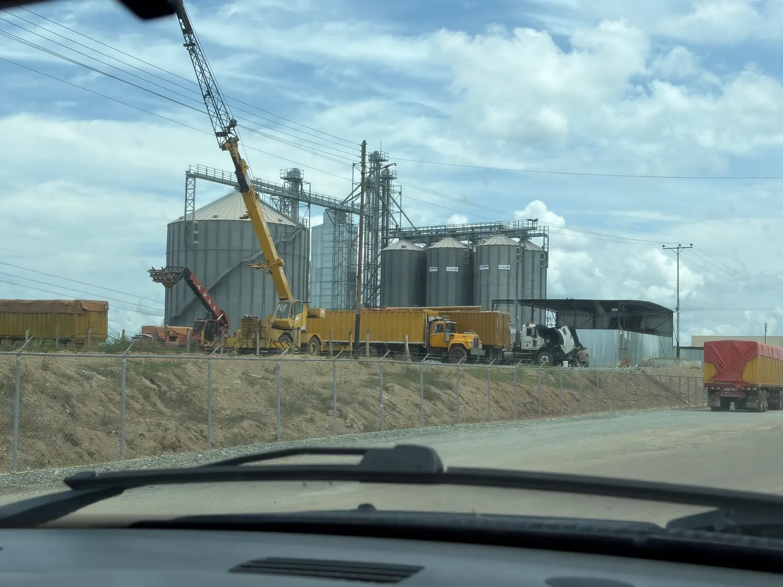 Silos de granos, camiones y una grúa vistos desde la carretera.